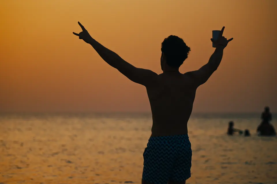 A guest raising both arms to the sunset at the water’s edge.